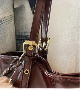 Close-up of glossy burgundy tote bag with gold hardware and plush pompom accessory