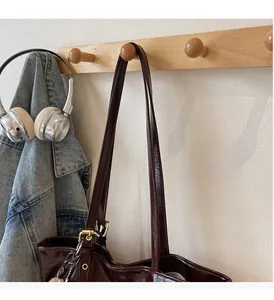 Detail of dark brown glossy leather tote bag showing handle and metal buckle on a wall hook