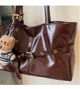 Detail of dark brown oil wax leather tote bag with metallic eyelets and plush bear charm