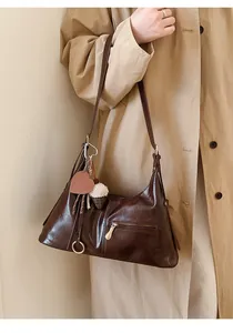 Détail du sac à bandoulière en cuir poli marron foncé avec boucles dorées et charms