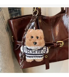 Detail of plush dog keychain with blue striped sweater on brown leather tote bag