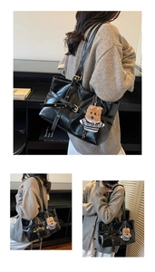 Detail of black glossy leather tote bag with silver eyelets and a plush bear charm