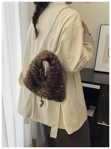 Detail of plush brown bucket bag with silver chain strap and golden ball pendant charm
