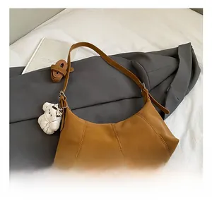Detail view of brown leather hobo bag with wide strap and plush bear charm accessory