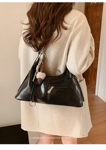 Détail du sac bandoulière noir brillant avec zip doré et charm gland en peluche sur manteau