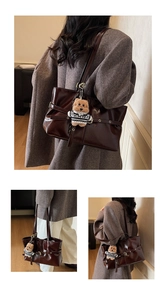 Detail of dark brown patent leather tote bag with buckle strap and cute bear charm