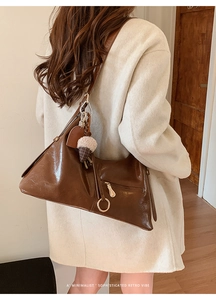 Sac fourre-tout marron avec pendentif porté sur un manteau en laine blanc