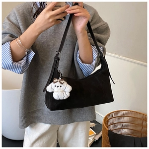 Close-up of black suede crescent shoulder bag with adjustable strap and cute plush dog charm