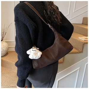 Detail of a dark brown crescent hobo bag with a cute plush charm on a model