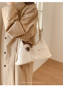 Détail du sac à main blanc crème avec fermeture éclair et gland sur un trench-coat kaki