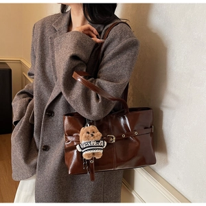 Sac cabas marron foncé brillant avec boucle et charm d'ours en peluche sur un modèle