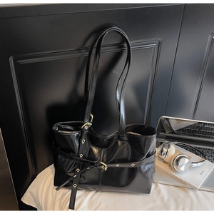 Détail du sac cabas en cuir ciré noir brillant avec boucle dorée et accessoires quotidiens