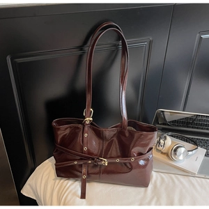 Détail de la texture cuir ciré brillant et boucle dorée sur un sac cabas rouge foncé