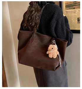 Detail of a large dark brown matte leather tote bag with a cute plush bear charm