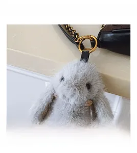 Close-up of grey plush bunny charm with gold chain on luxury leather baguette handbag