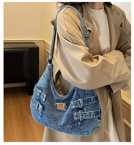Détail du sac hobo en jean vintage avec boucles métalliques et plaque dorée sur tissu bleu