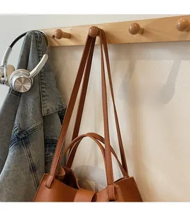Brown lychee texture leather tote bag hanging on a wooden hook with denim jacket