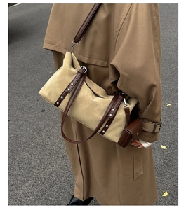 Detail of beige suede barrel bag with brown leather straps and silver studs on a street