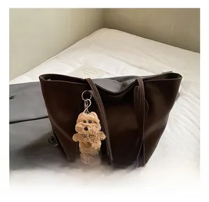 Detail view of large dark brown tote bag with plush puppy pendant on white background
