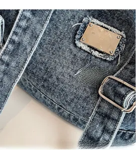 Détail d'un sac en denim délavé montrant la plaque en métal argenté et le bord effiloché