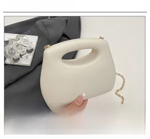 Detalle de bolso de acrílico blanco roto con cadena dorada sobre blazer gris