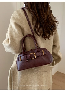 Detail of burgundy minimalist retro handbag showing gold hardware on beige wool coat
