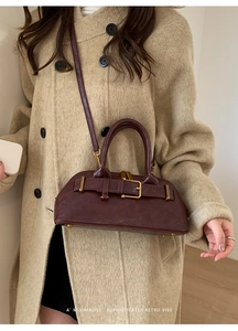 Close-up of a burgundy leather retro handbag with golden metal buckle on a neutral coat