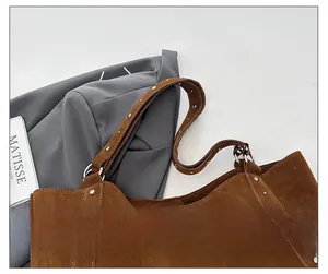 Détail du sac bandoulière en daim marron avec rivets métalliques argentés sur la sangle