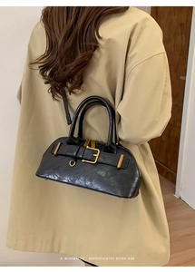 Detail showing glossy black leather texture and gold buckle on a retro shoulder bag