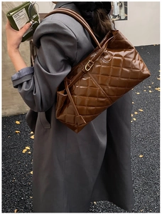 Close-up of brown quilted faux leather tote bag with gold buckle on shoulder strap