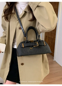 Detail of minimalist black retro handbag with gold buckle on a stylish trench coat outfit