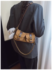 Detail of brown suede dumpling bag featuring front pockets with metal buckles and plush charm