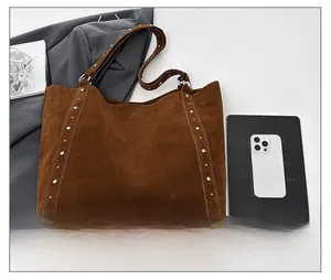 Détail d'un grand cabas en daim marron avec rivets argentés et boucle métallique