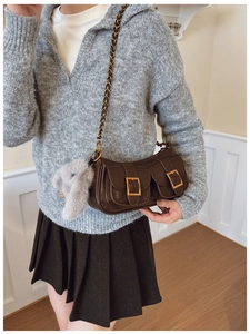 Detail of a brown leather shoulder bag with gold buckles, chain strap, and plush charm