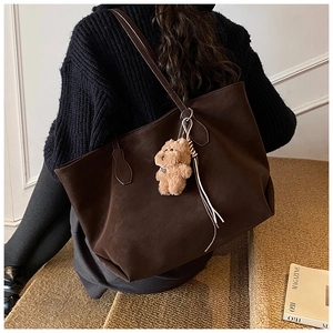 Brown faux suede tote bag with plush puppy charm shown on a model sitting on steps