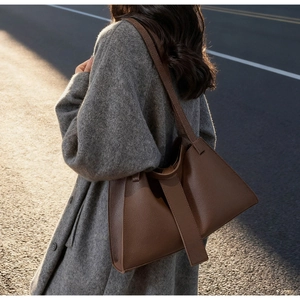 Detail of dark brown pebble leather tote bag with wide strap on grey wool coat