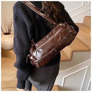 Detail of dark brown high-gloss leather bowling bag with punk metal zippers and eyelet straps