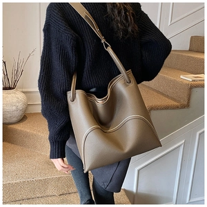 Detail view of taupe lychee leather tote bag with contrast white stitching on a model