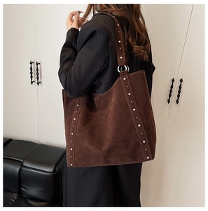 Détail de rivets argentés sur un sac cabas en daim marron foncé avec texture en cuir