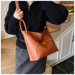 Detail view of large brown leather bucket bag with contrasting stitching on a model