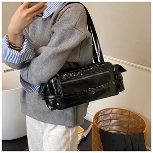 Model wearing a black glossy retro shoulder bag with zipper and buckle detail