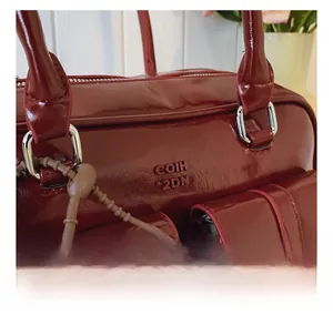 Détail du sac bandoulière en cuir verni rouge foncé avec anneau argenté et logo COIH 2DN