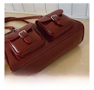 Gros plan du sac bandoulière en cuir verni bordeaux avec poches à boucles argentées