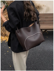 Detail of dark brown lychee leather tote bag featuring elegant white piping decoration