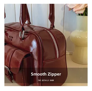 Détail du sac à main en cuir verni bordeaux avec fermeture éclair fluide et poche à boucle