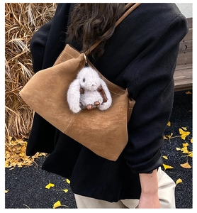 Brown suede tote bag detail with white stitching and grey rabbit charm in autumn setting
