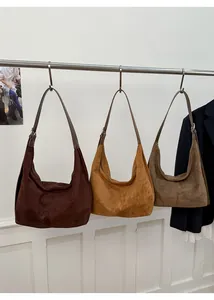Three minimalist suede tote bags in brown, caramel, and olive hanging on a display rack