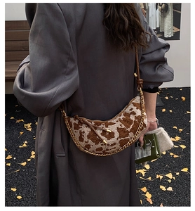 Detail of moon bag with cow print fabric, gold chain, and leather strap in autumn setting