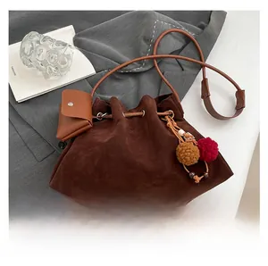 Detail of dark brown suede bucket bag with drawstring closure and colorful pompom charm