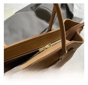 Close-up of golden metal zipper and stitching details on a brown leather tote bag
